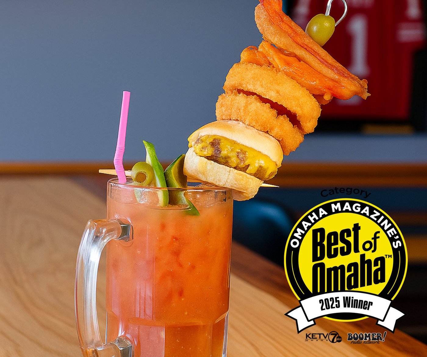 Report In Pub's award-winning Giant Bloody Mary — topped with a slider, onion rings, bacon, and an olive — Best of Omaha 2025 Winner